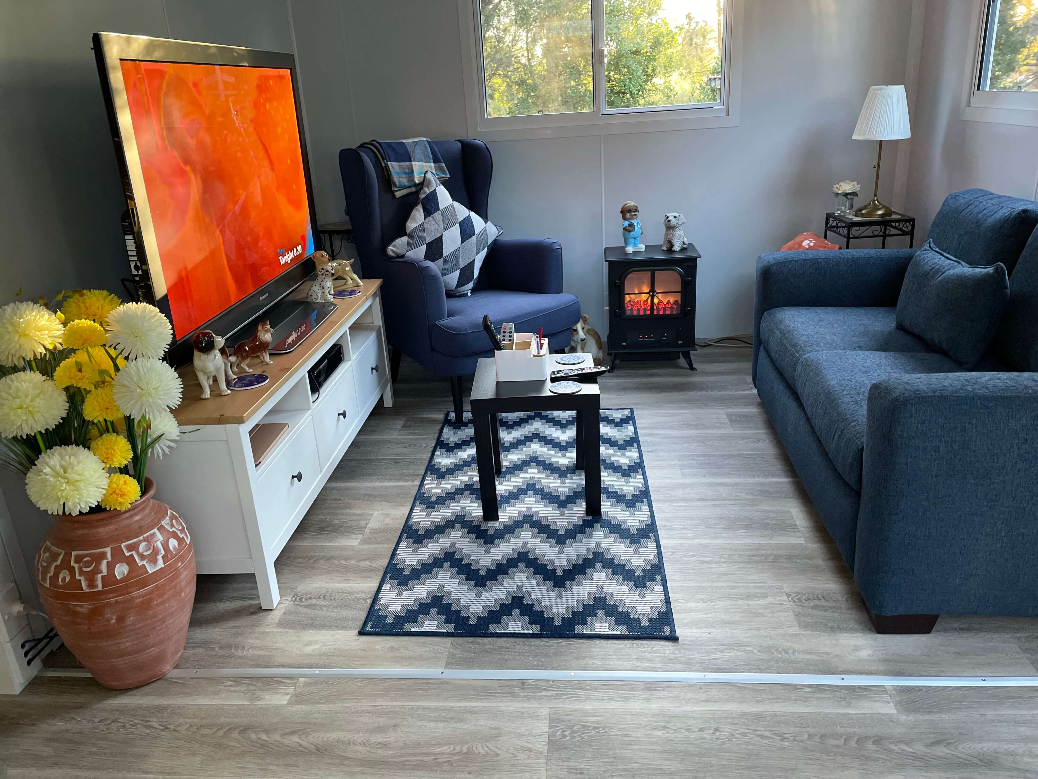 VanHomes - A cosy lounge room with a plush sofa, patterned rug, and a fireplace.